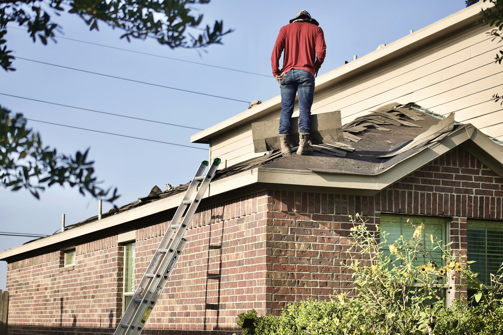 A roofer tearing off old shingles on a brick home roof in Mississippi